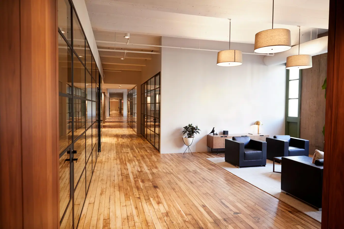 Office hallway with glass walls, wood floor and lounge chairs